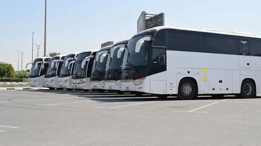 Fleet of white luxury coaches parked in a row at an outdoor lot in Abu Dhabi under clear blue sky.