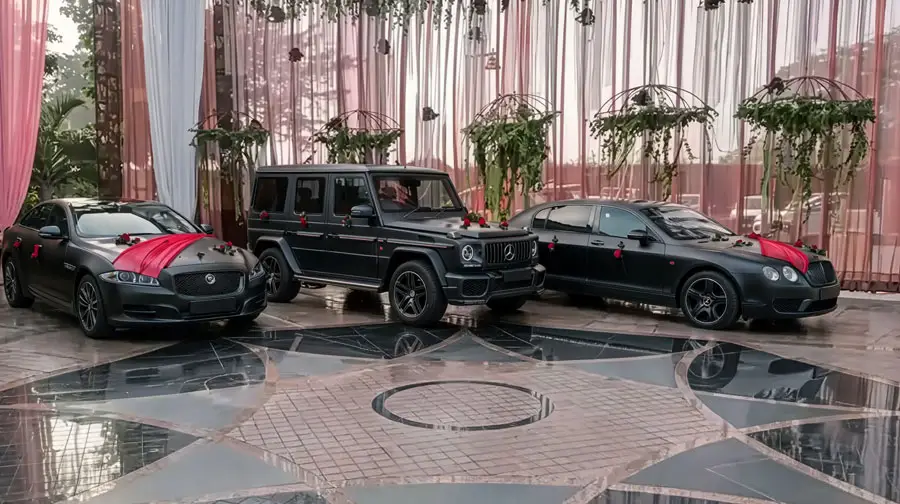 Three black luxury cars (Jaguar, Mercedes G-Class, and Bentley) decorated with red ribbons and flowers parked at a wedding venue in Abu Dhabi.