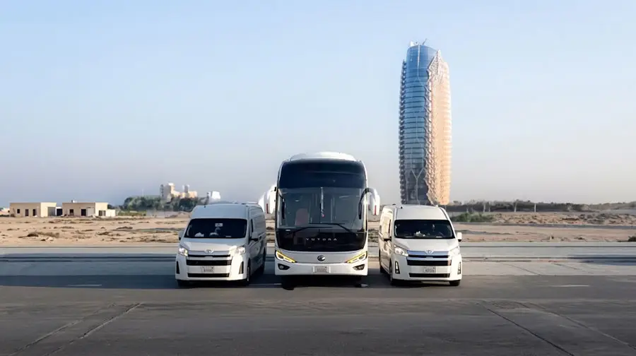 Fleet of white luxury vans and Yutong coach for large group airport transfers in Abu Dhabi.