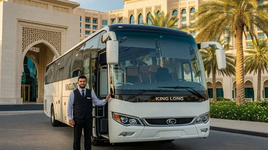 King Long luxury coach parked at a premium hotel in Abu Dhabi with uniformed chauffeur ready for group airport transfer service.