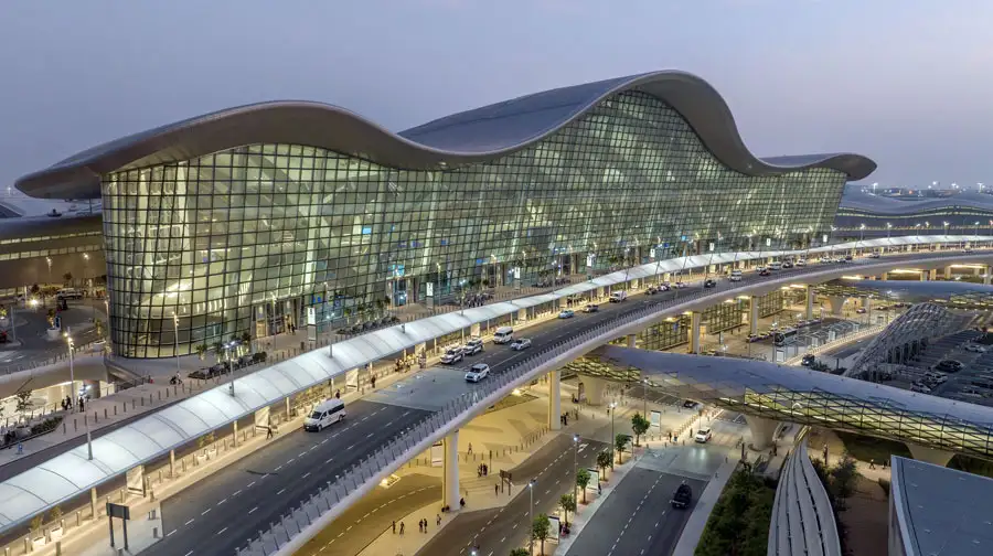 A high-angle wide shot of the Zayed International Airport (formerly Abu Dhabi International) Terminal A at dusk.
