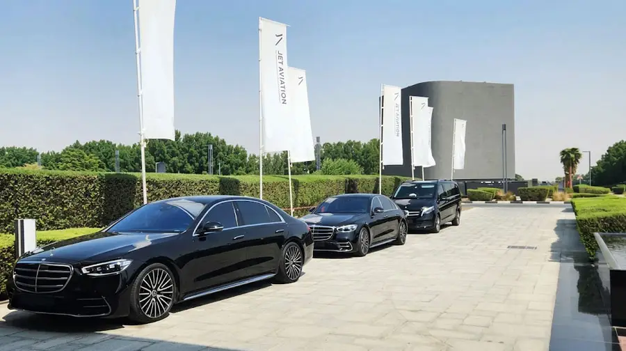 Executive fleet of black Mercedes-Benz S-Class luxury sedans and VIP van parked along a driveway with Jet Aviation flags in Abu Dhabi.