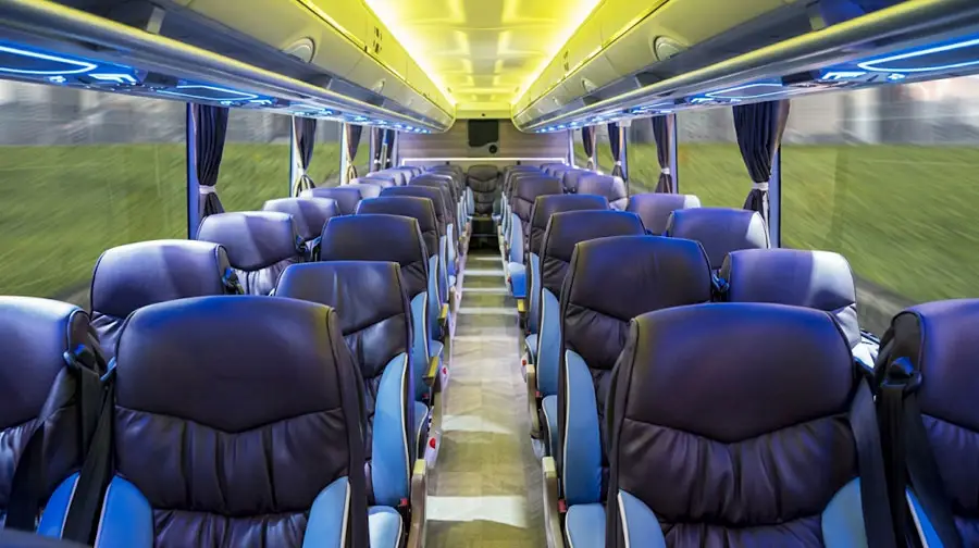 Interior view of a luxury passenger coach featuring blue and black leather seating, an aisle, and ambient overhead lighting.