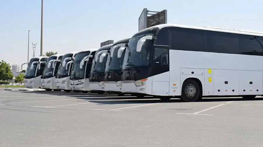 A lineup of white charter buses parked in a outdoor parking lot on a sunny day in Abu Dhabi.