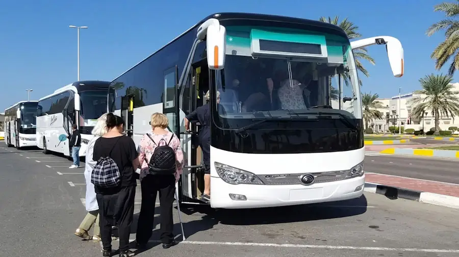 Tourists queuing up to board a white luxury tour bus in Abu Dhabi.
