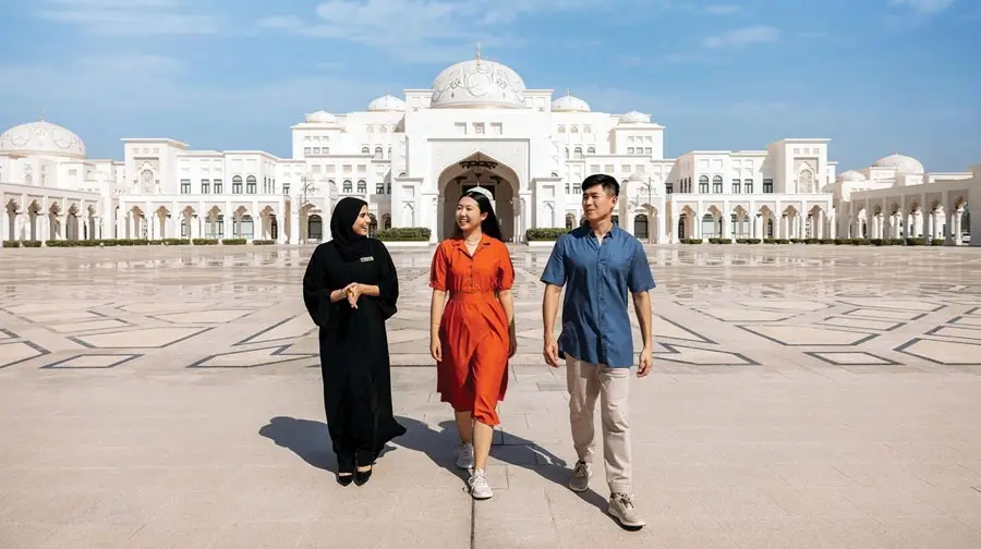 Tour guide in traditional abaya walking with visitors across the grand courtyard of Qasr Al Watan in Abu Dhabi.